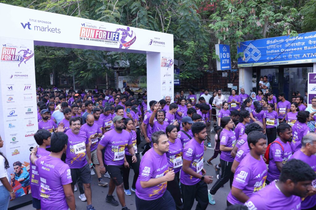 Crowd of runners in purple shirts gather at a marathon start under a sponsor banner reading Run for Life 3K  5K i